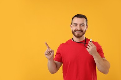 Photo of Happy young man with whistle on orange background, space for text