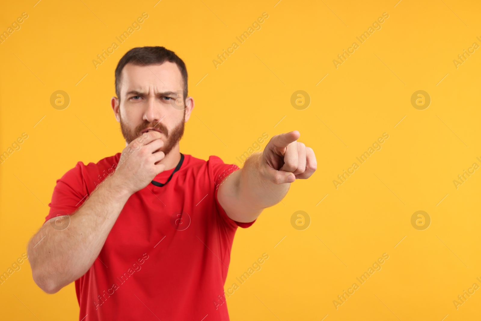 Photo of Young man blowing whistle on orange background, space for text