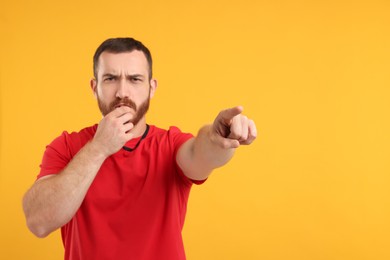 Photo of Young man blowing whistle on orange background, space for text