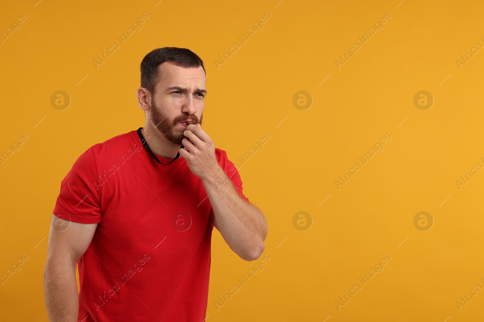 Photo of Young man blowing whistle on orange background, space for text