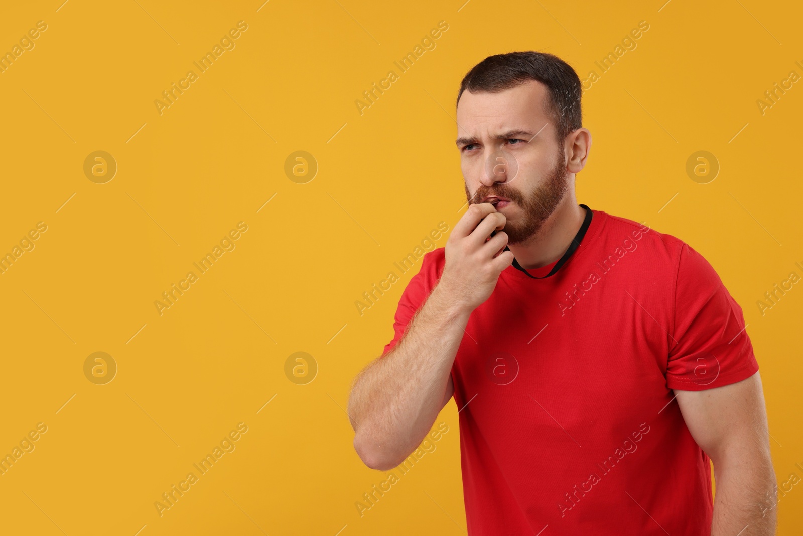 Photo of Young man blowing whistle on orange background, space for text