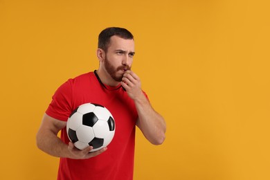 Photo of Young man with soccer ball blowing whistle on orange background, space for text