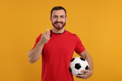 Photo of Happy young man with whistle and soccer ball on orange background