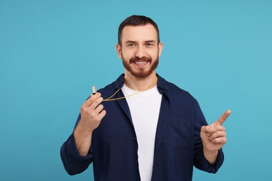 Happy young man with whistle on light blue background