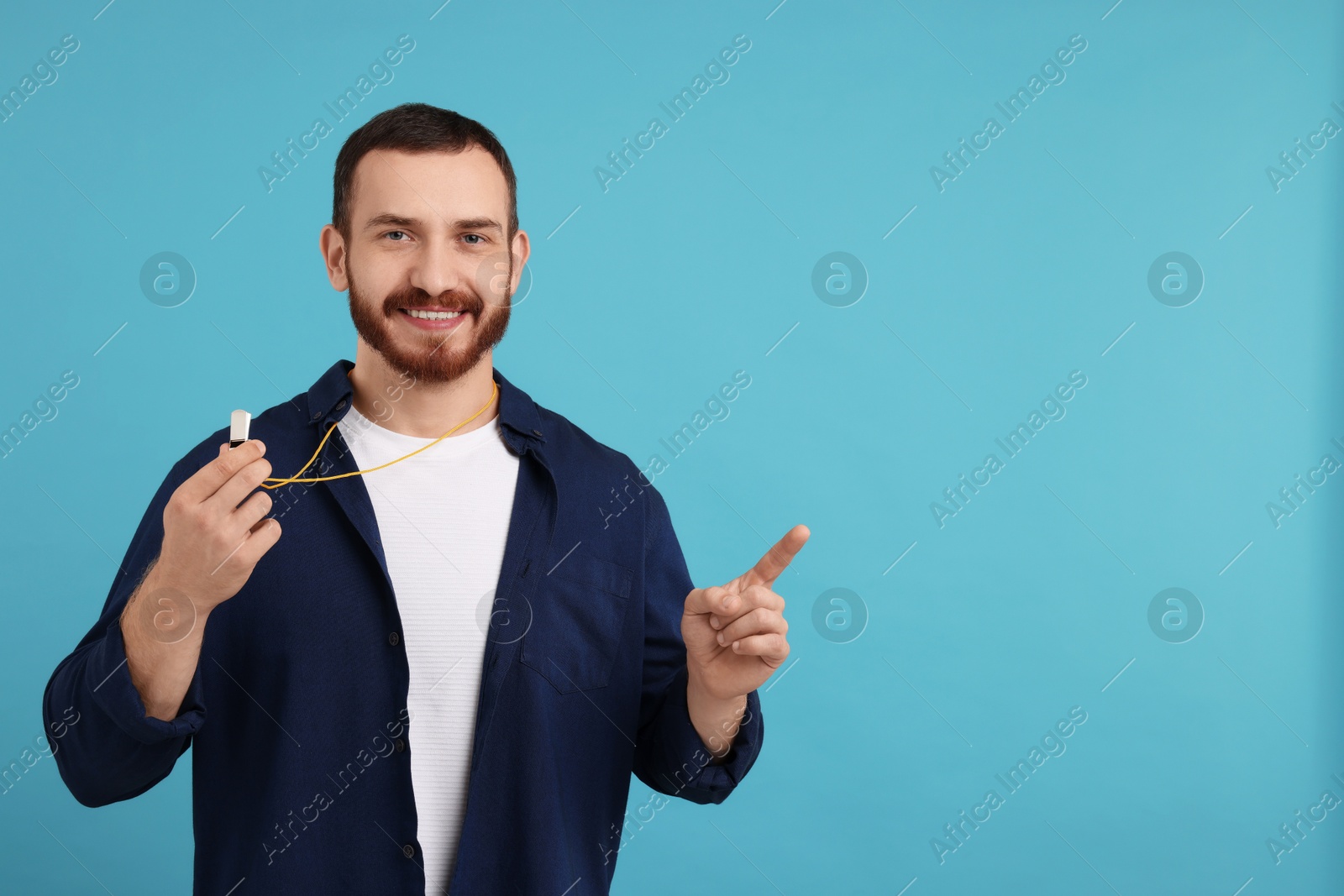 Photo of Happy young man with whistle on light blue background, space for text