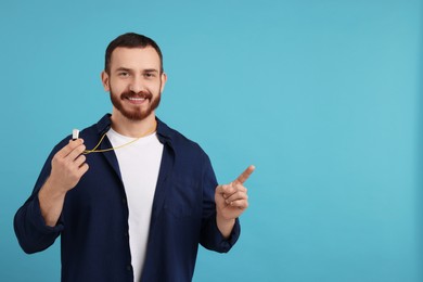 Photo of Happy young man with whistle on light blue background, space for text