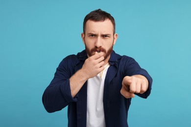 Photo of Young man blowing whistle on light blue background