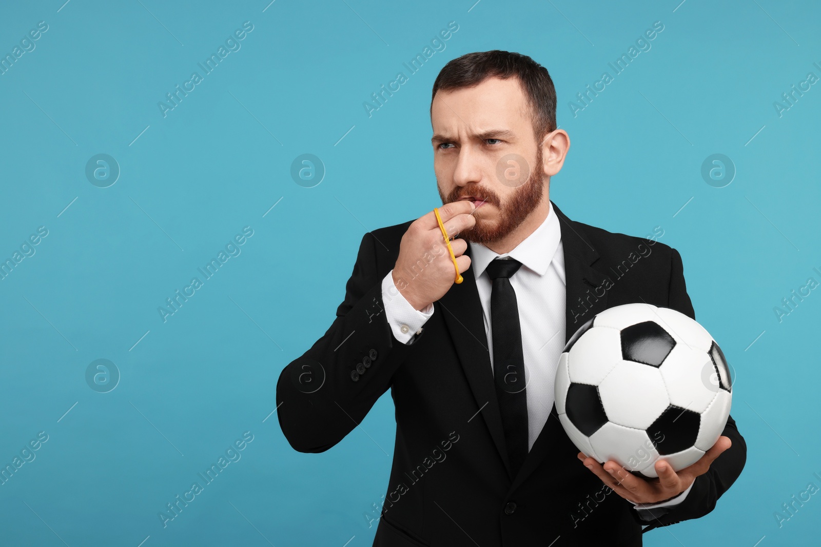 Photo of Young man with soccer ball blowing whistle on light blue background, space for text