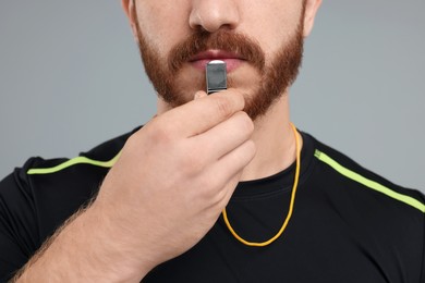 Photo of Man blowing whistle on grey background, closeup