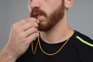 Photo of Man blowing whistle on grey background, closeup