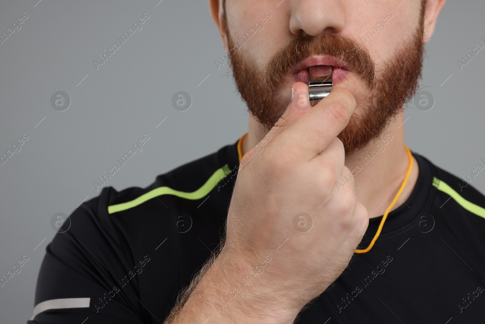 Photo of Man blowing whistle on grey background, closeup