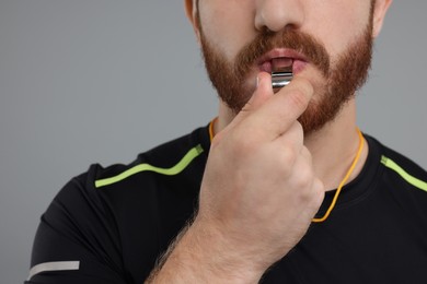 Photo of Man blowing whistle on grey background, closeup