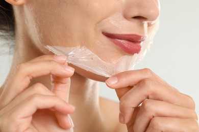 Photo of Woman peeling off face mask on light grey background, closeup