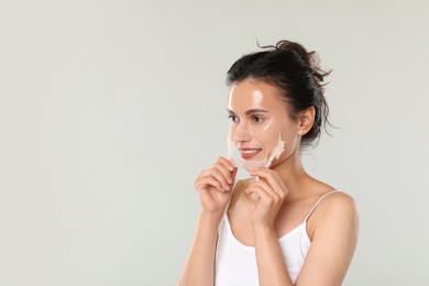 Smiling woman peeling off face mask on light grey background. Space for text