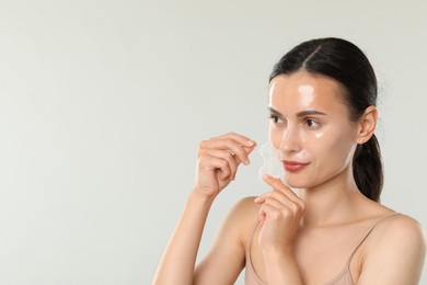 Beautiful woman peeling off face mask on light grey background. Space for text