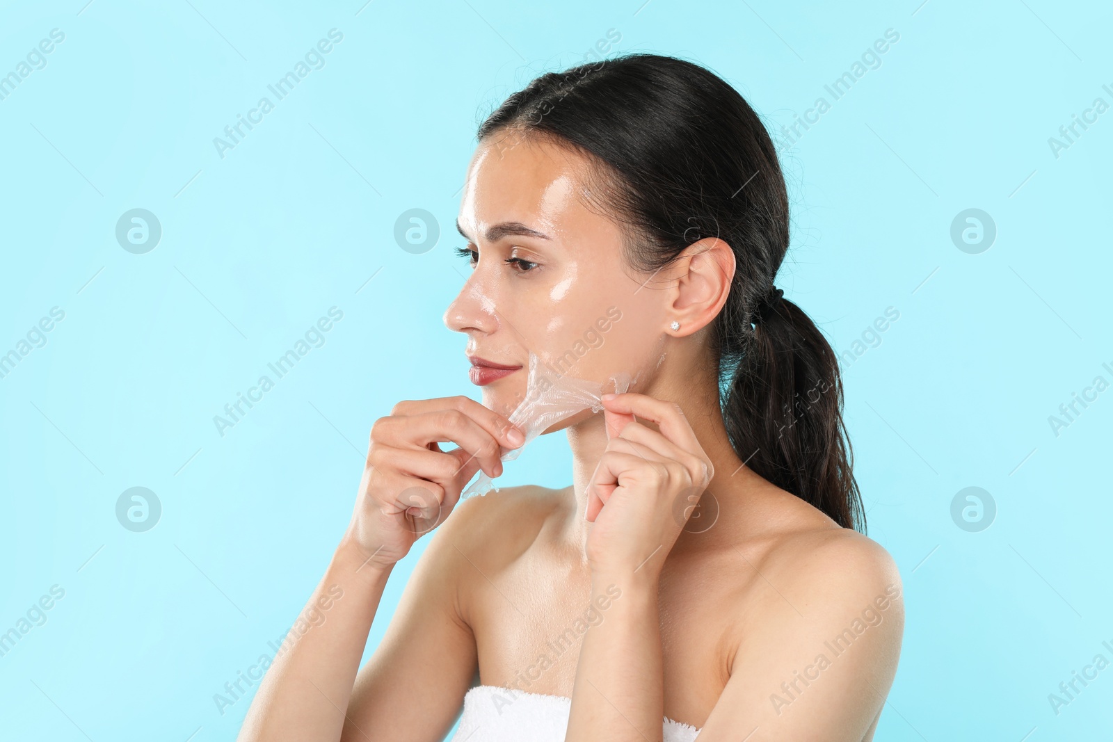 Photo of Beautiful woman peeling off face mask on light blue background