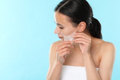 Beautiful woman peeling off face mask on light blue background. Space for text