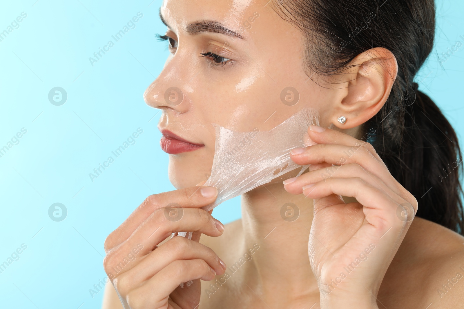 Photo of Beautiful woman peeling off face mask on light blue background, closeup