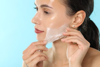 Photo of Beautiful woman peeling off face mask on light blue background, closeup