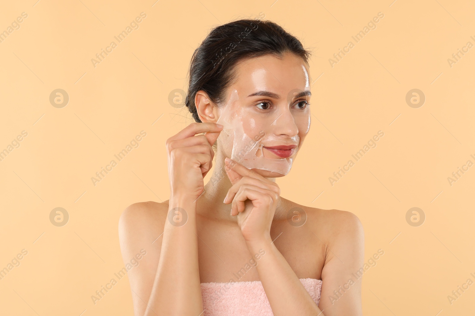 Photo of Beautiful woman peeling off face mask on beige background