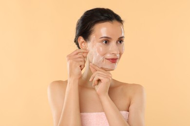 Beautiful woman peeling off face mask on beige background