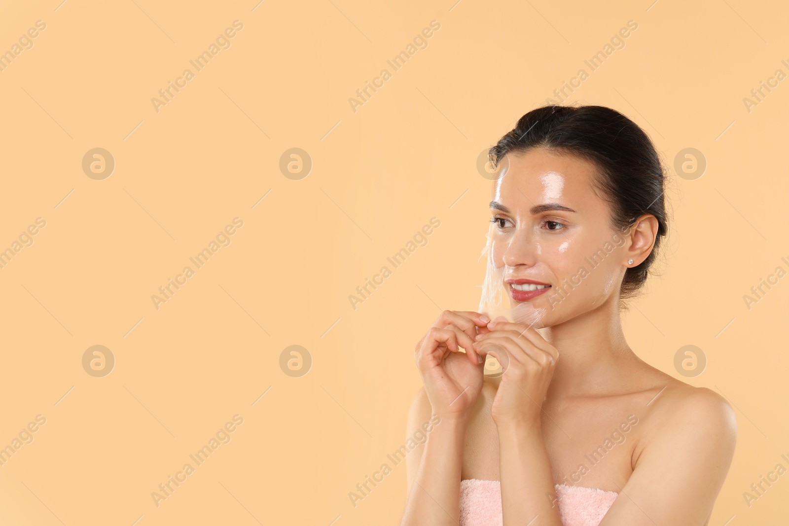 Photo of Beautiful woman peeling off face mask on beige background. Space for text