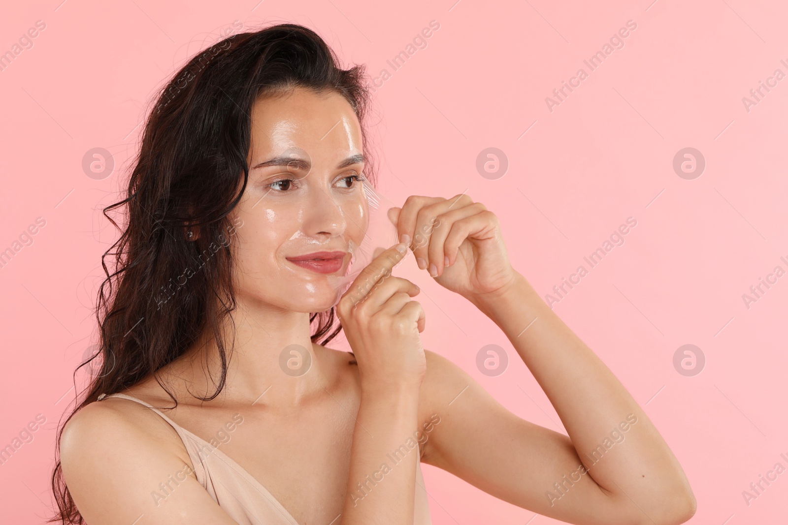 Photo of Beautiful woman peeling off face mask on pink background