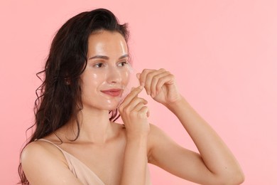 Beautiful woman peeling off face mask on pink background