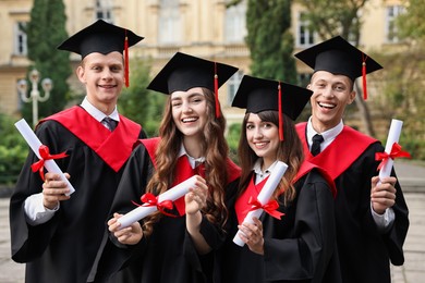 Happy students with diplomas after graduation ceremony outdoors