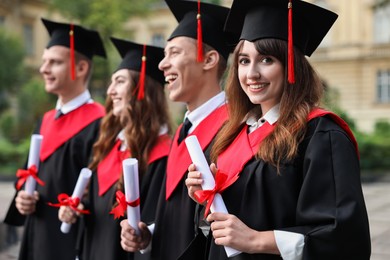 Happy students with diplomas after graduation ceremony outdoors, selective focus