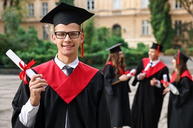 Photo of Happy students with diplomas after graduation ceremony outdoors, selective focus