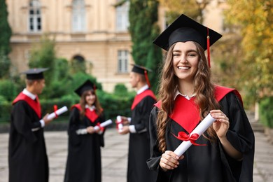 Photo of Happy students with diplomas after graduation ceremony outdoors, selective focus