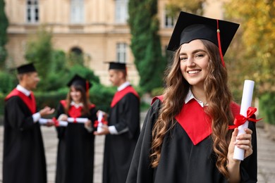 Happy students with diplomas after graduation ceremony outdoors, selective focus