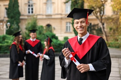 Photo of Happy students with diplomas after graduation ceremony outdoors, selective focus