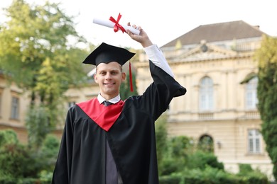 Happy student with diploma after graduation ceremony outdoors, space for text