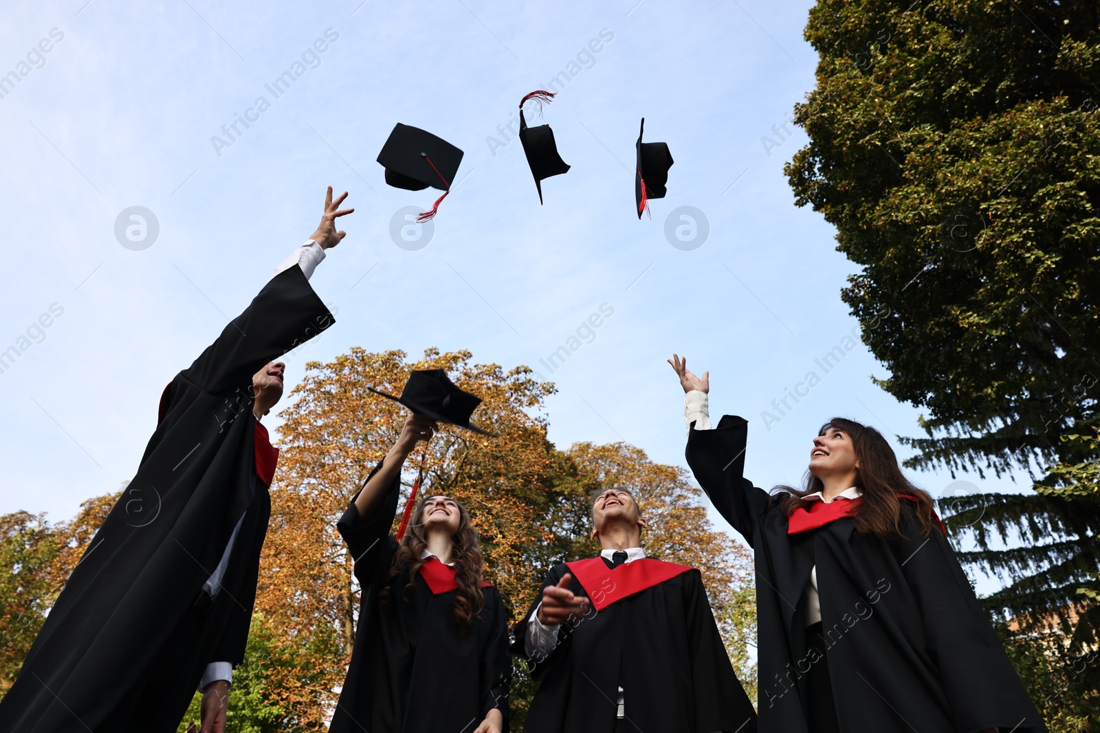 Photo of Graduation ceremony. Group of students throwing hats outdoors, low angle view