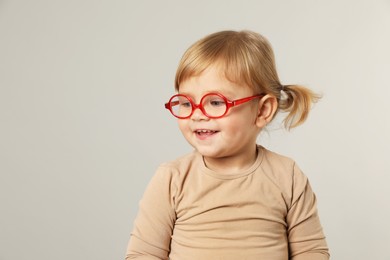 Cute little girl in glasses on light grey background. Space for text