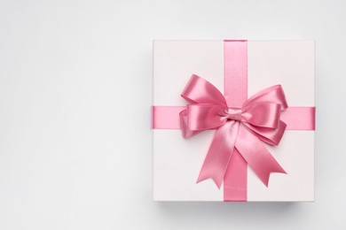 Photo of Gift box with pink bow on light grey background, top view. Space for text