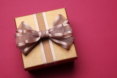 Photo of Gift box with bow on burgundy background, above view. Space for text