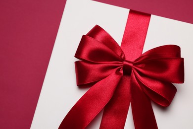 Photo of Gift box with red bow on burgundy background, above view