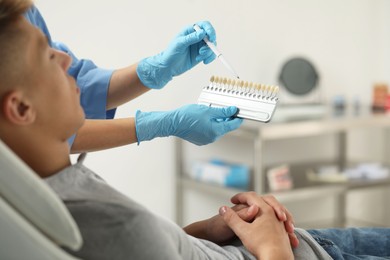 Photo of Doctor and patient choosing shade on teeth color palette in clinic, closeup. Dental veneers