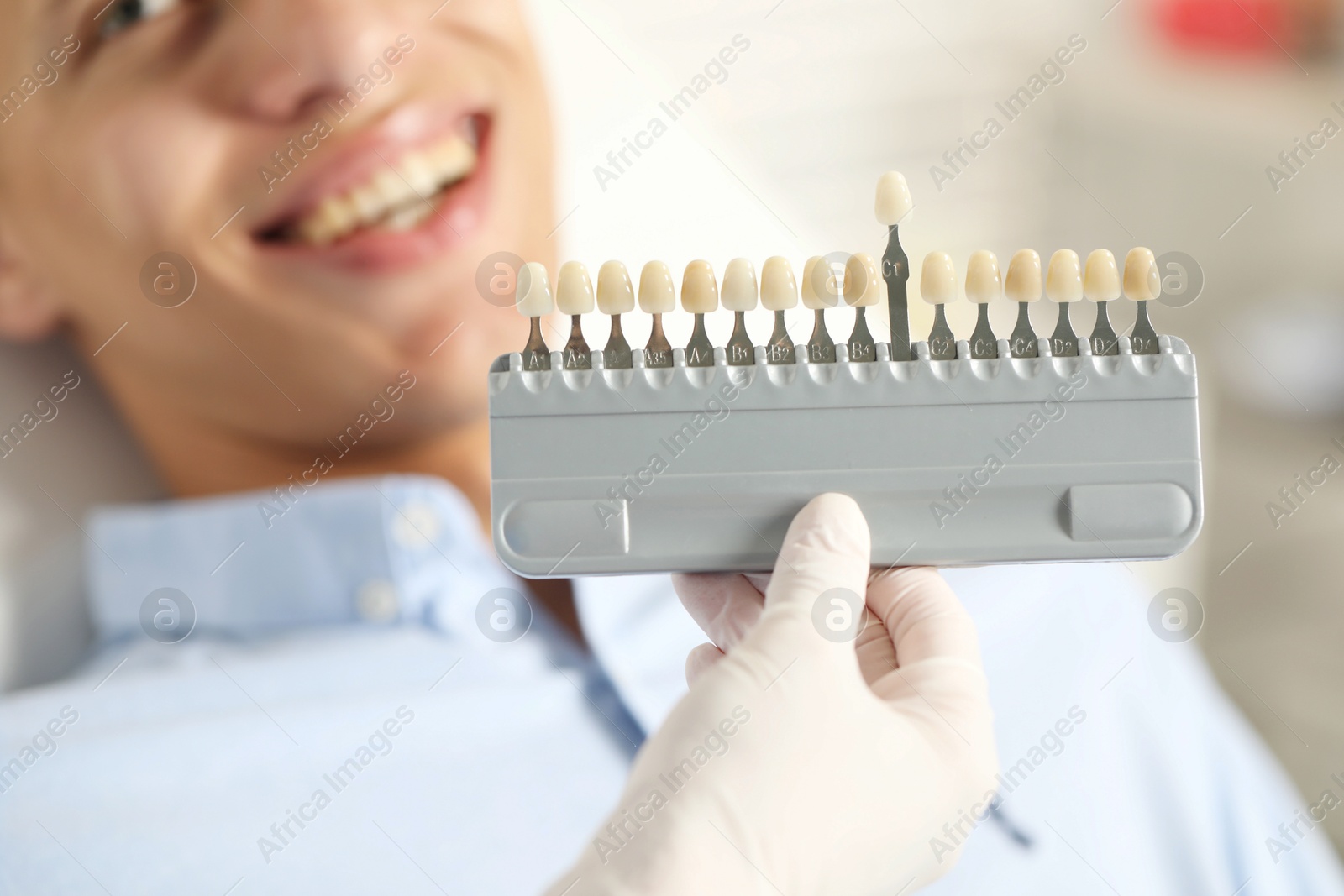 Photo of Happy young man and doctor with teeth color chart in clinic, selective focus. Dental veneers