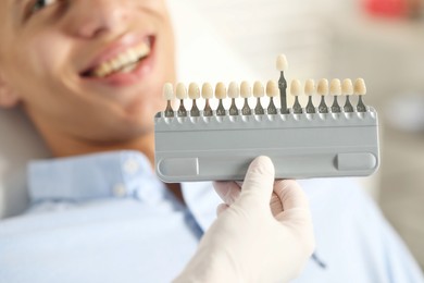 Photo of Happy young man and doctor with teeth color chart in clinic, selective focus. Dental veneers