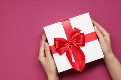 Photo of Woman holding gift box with bow on dark rose background, top view