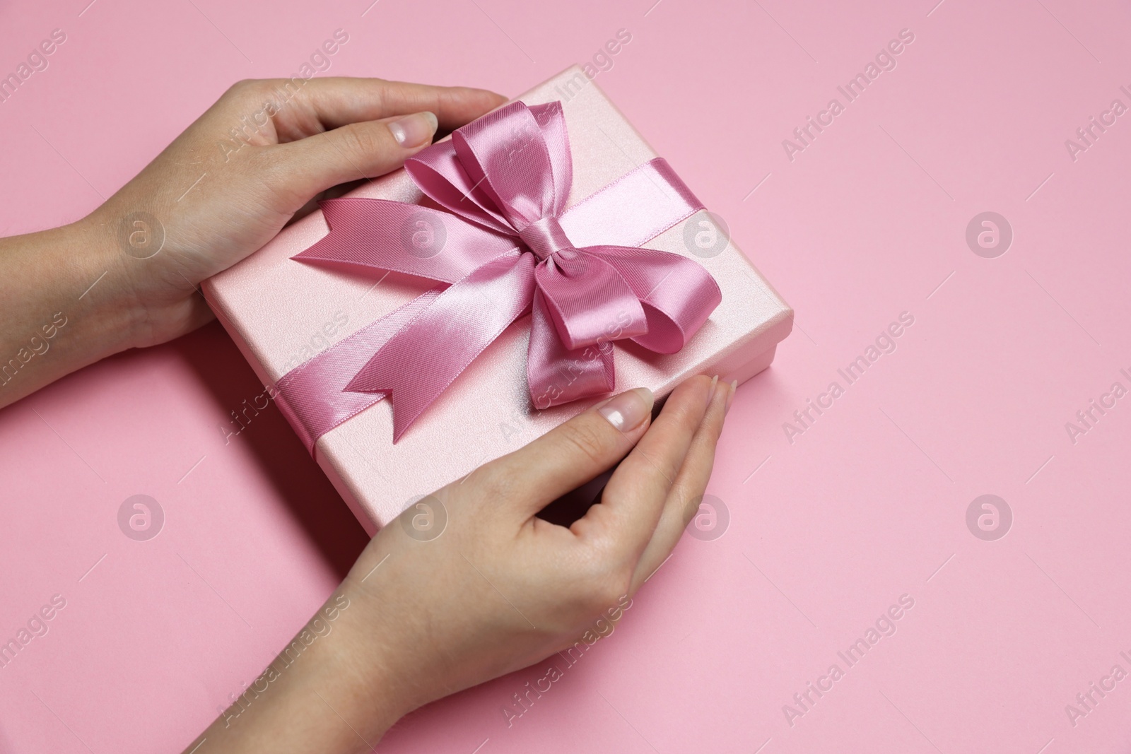 Photo of Woman holding gift box with bow on pink background, closeup