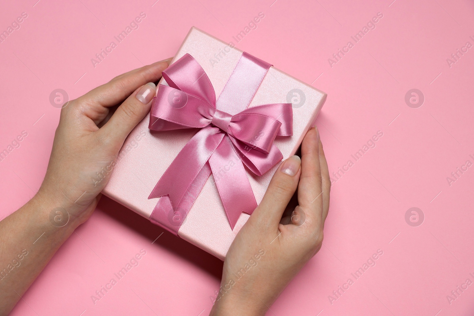 Photo of Woman holding gift box with bow on pink background, top view