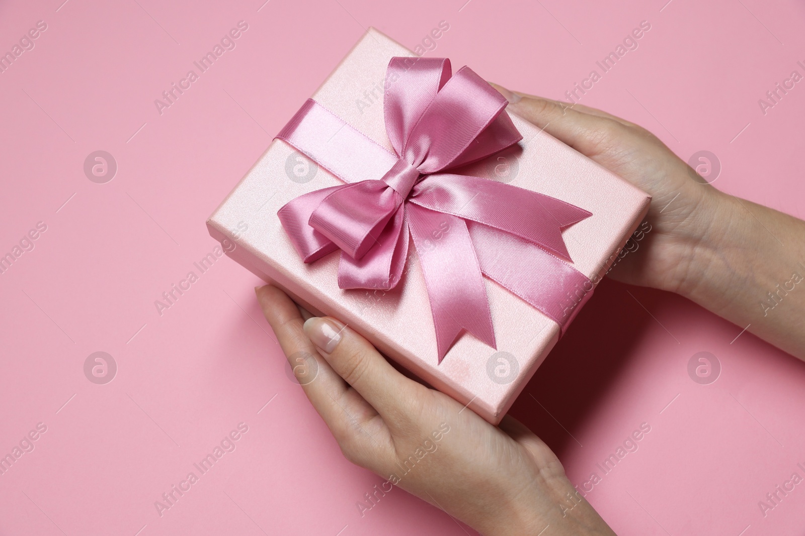 Photo of Woman holding gift box with bow on pink background, closeup