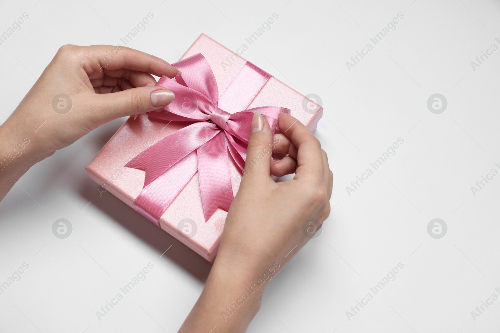 Photo of Woman decorating gift box with bow on white background, closeup