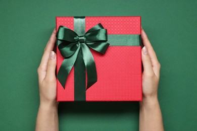 Photo of Woman holding gift box with bow on green background, top view