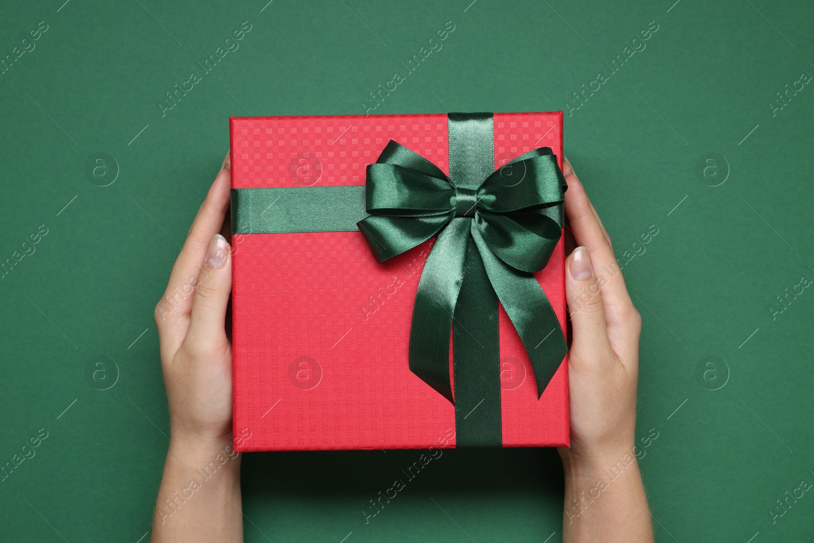 Photo of Woman holding gift box with bow on green background, top view